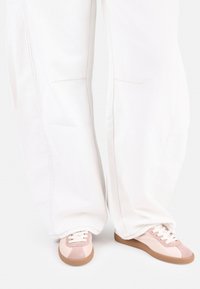Pink and beige sneakers with a suede and fabric upper, lace closure, and textured rubber sole, paired with white loose-fitting pants.