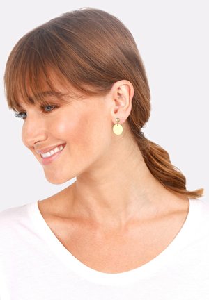 Pendientes en tono dorado que presentan un pequeño botón de perla y un disco redondo colgante de color amarillo claro, sobre un fondo neutro.