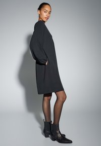 Zwarte jurk met lange mouwen en zijzakken, met een comfortabele pasvorm. Paar zwarte enkellaarsjes met vierkante hakken en elastische zijkanten.