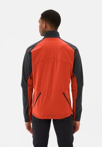 Rote und schwarze Softshell-Jacke mit hohem Kragen, Reißverschluss-Seitentaschen und kontrastierenden Schulterakzenten. Glatte Textur, taillierte Passform.