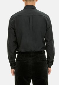 Zwarte lange mouw shirt met een knoopkraag en rugplooien, gecombineerd met gestructureerde zwarte corduroy broek met achterzakken.