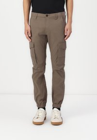 Pantalones cargo en marrón claro, con puños elásticos, bolsillos laterales y un corte regular. Fabricados con una tela resistente de textura suave.