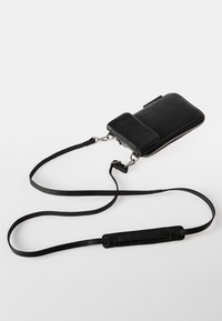 Zwarte leren telefoontas met een ritsluiting, afneembare schouderband en een klein voorvak. Soepele textuur en minimalistisch ontwerp.