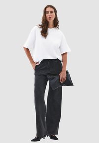 Losse witte katoenen T-shirt, grafietkleurige broek met brede pijpen en drawstring, en een zwarte leren clutch. Textuur en kleurcontrast zijn duidelijk zichtbaar.