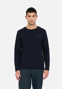 Maglietta a maniche lunghe di colore navy realizzata in morbido tessuto, caratterizzata da un colletto rotondo e un piccolo logo sul petto. Texture liscia e vestibilità regolare.