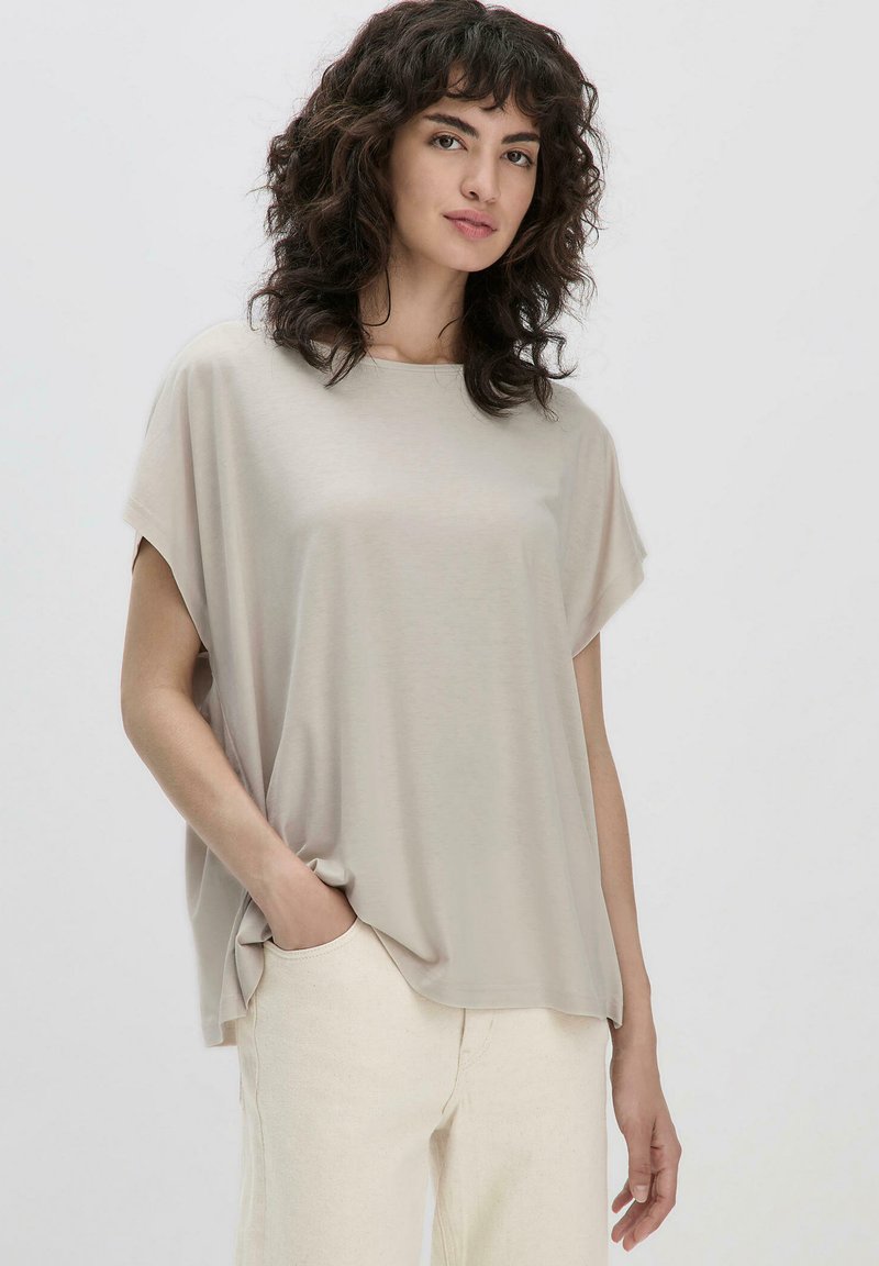 Beige, locker sitzendes Oberteil mit kurzen Ärmeln, runder Ausschnitt und weicher Textur, kombiniert mit hellen Hosen. Minimalistisches Design, ohne Muster.