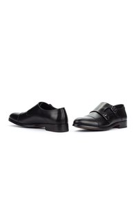 Un par de zapato formal de cuero negro con hebillas dobles en un fondo blanco.