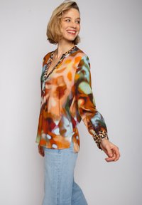 Seidenbluse mit einem orange-, blau- und grünfarbenen abstrakten Muster, V-Ausschnitt und Leopardenmuster-Akzenten an den Manschetten und dem Kragen.