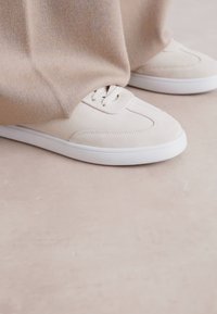 Sneaker in suede beige con suole in gomma bianca, dal design minimalista, punta rotonda e dettagli di cucitura sottili.