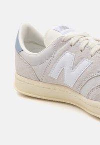 Adidași gri și albi, realizati din suede și piele, cu un logo alb „N” proeminent, textura moale și un accent albastru deschis la toc.