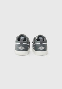 Baskets en cuir gris avec semelles blanches, col rembourré et brides Velcro ajustables. Présentent un talon texturé et un détail de logo sur le côté.
