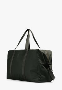 Bolsa de lona grande de color verde oscuro, hecha de tela, con asas reforzadas, cierre de cremallera y una correa de hombro desmontable.