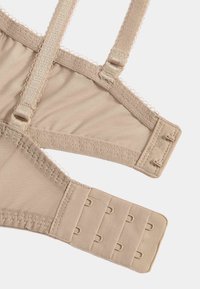 Fragmento de sujetador beige con textura suave, tirantes ajustables y cierre de gancho y ojo con tres filas de ganchos.