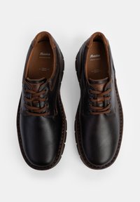 Crne kožne cipele s glatkom površinom i smešnim naglascima. Imaju okrugli vrh, vezivanje na šest rupa i teksturiranu gumenu petu.