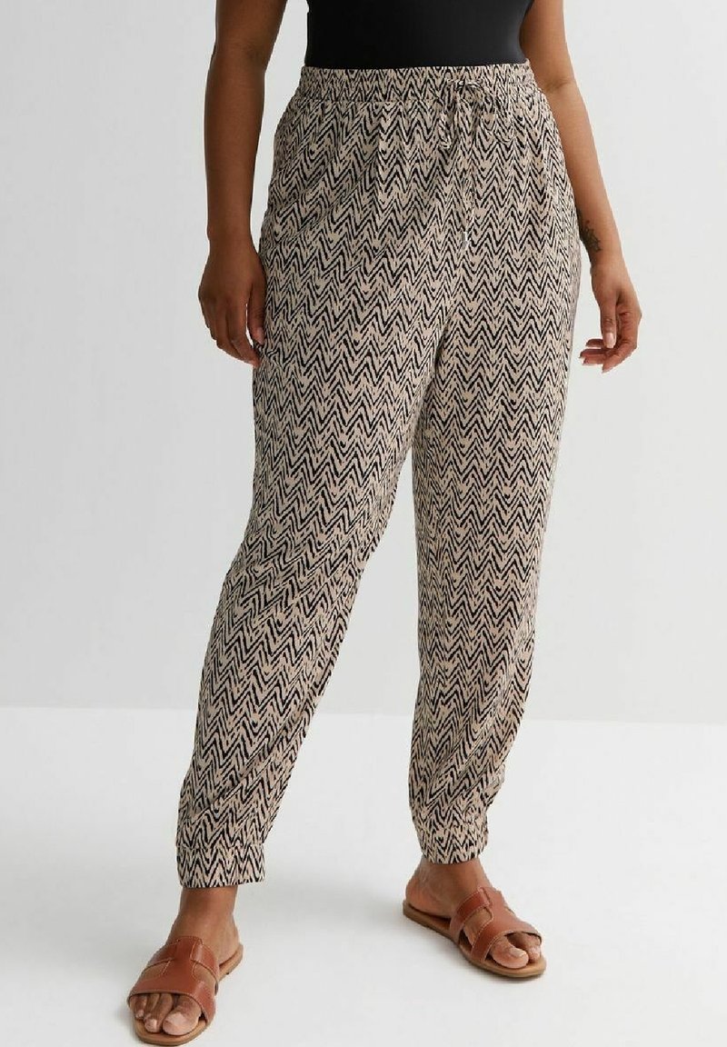 Leichte, gemusterte Hosen mit einem schwarzen Zickzackdesign auf beigem Hintergrund. Elastischer Bund, schmal zulaufende Beine und Seitentaschen.