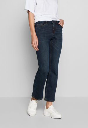 Granatowe dżinsy o prostym kroju, z kontrastowym przeszyciem i pięcioma kieszeniami, noszone z białymi trampkami.