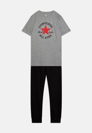 Graues kurzärmliges T-Shirt mit einem roten Stern-Graphic und schwarzem Text, kombiniert mit schwarzen schmalen Jogginghosen mit elastischen Bündchen.