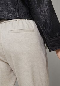 Schwarze Lederjacke kombiniert mit hellgrauen Sweatpants, die eine strukturierte Oberfläche und ein verstecktes Taschen-detail auf der Rückseite aufweisen.