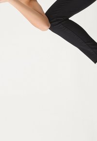 Pantalones ajustados negros con una textura suave, sin patrones visibles y una silueta elegante, presentados sobre un fondo blanco liso.