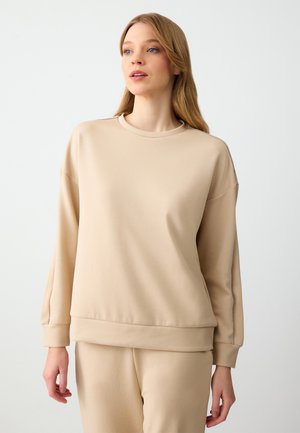 Sweatshirt beige con finitura testurizzata, scollatura rotonda e spalle scese. Il design minimalista presenta dettagli di cucitura sottili e polsini a costine.