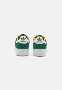 Green suede sneakers with white rubber soles, yellow and green interior, and Adidas logo on the back, featuring a classic silhouette.