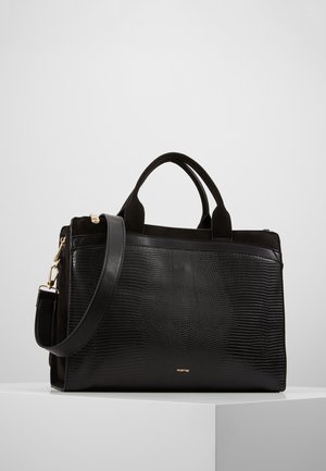 Sac à main en cuir noir texturé avec deux poignées et une bandoulière amovible reposant sur une surface blanche sur un fond uni.