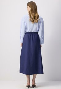 Cămașă albastră cu mâneci lungi, asociată cu o fustă lungă până la gleznă, de culoare bleumarin, care dispune de un brâu elastic. Fusta are o textură netedă și o croială lejeră.