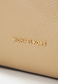 Sac à main en cuir beige avec une finition texturée, arborant un accent doré au logo "MICHAEL KORS". Design simple sans embellissements supplémentaires.