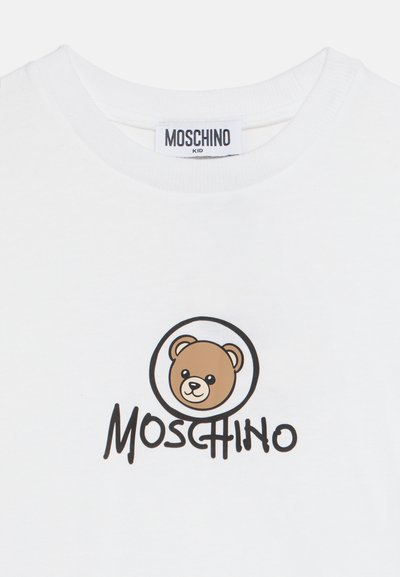 Λευκό παιδικό T-shirt Moschino με πρόσωπο αρκουδάκι μέσα σε κύκλο και το όνομα της μάρκας γραμμένο κάτω σε μαύρα γράμματα.