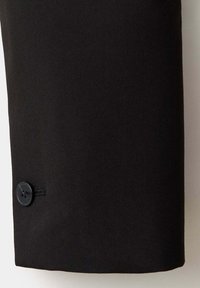 Manche en tissu noir avec un seul bouton foncé cousu près du poignet, présentée sur un fond clair.