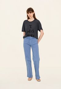 Šedé tričko s černým textem "Byl jsem tu", spárované s světle modrými širokými kalhotami. Jednoduchý design, krátké rukávy, jemná textura.