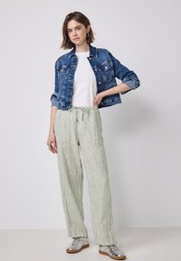 Džínová bunda, bílý tričko, pruhované zelené široké kalhoty, stříbrné tenisky. Neformální outfit s volným střihem a měkkými texturami.