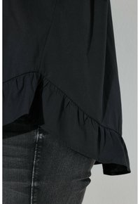 Black top with a ruffled hem, made from a soft, smooth fabric. Paired with dark, fitted jeans, highlighting the garment's shape.
