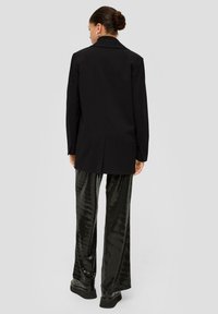 Black blazer with a tailored fit, featuring a back vent. Paired with shiny black sequin pants and platform shoes.
