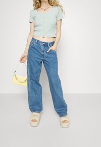 Světle modrý žebrovaný zkrácený top s knoflíky, v kombinaci s volnými modrými džíny. Modelka drží malou žlutou kabelku. Měkké béžové platformové sandály.