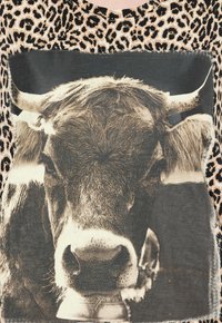 Halenka s leopardím potiskem, která má centrální černobílou grafiku krávy. Materiál je měkký s třepenými okraji a kulatým výstřihem.