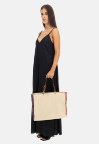 Borsa a spalla in tela crema con accenti viola e arancione, presenta manici in pelle marrone e accessori in argento. Forma rettangolare, design robusto.