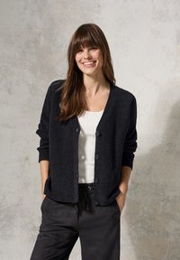 Dunkel gestrickte Cardigan mit strukturiertem Finish, mit Knopfverschluss und gerippten Bündchen, kombiniert mit einem weißen Hemd und dunklen Hosen.