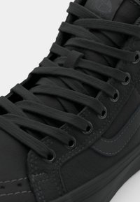 Black high-top sneaker made of smooth leather. Features flat black laces, textured upper, and subtle contrasting stitching detail.