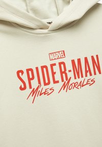 Beige huppari pehmeällä pinnalla, jossa on rohkeat punaiset "SPIDER-MAN" ja "Miles Morales" grafiikat, ja pieni "MARVEL" logo ylhäällä.