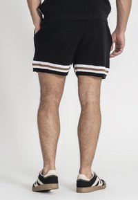 Shorts neri in maglia con bordo a strisce bianche e marroni in contrasto all'orlo. Indossati con sneakers nere e crema.