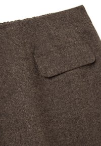 Tissu marron texturé avec une poche rectangulaire à rabat cousue, mettant en valeur un tissage détaillé et des bords de coutures.