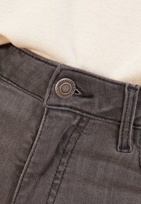 Šedé džíny z denimu s kovovým knoflíkem s nápisem "Hugo Boss", viditelným švem a hladkým povrchem na pasu.