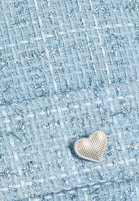 Tessuto intrecciato di colore azzurro chiaro con una finitura testurizzata, caratterizzato da un piccolo accento a forma di cuore in argento. I motivi includono un design a scacchi con fili metallici.