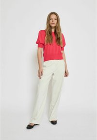 Top en tricot fuchsia avec des manches bouffantes et un ourlet côtelé, associé à un pantalon large blanc et des ballerines noires. Lignes simples et épurées, textures douces.