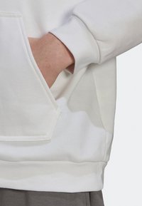 Sweatshirt blanc avec une poche avant, fabriqué en tissu doux. Présente un poignet et un ourlet côtelés, mettant en avant une coupe décontractée et une texture lisse.