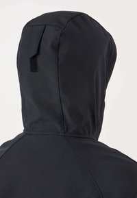 Juodas gobtuvuotas švarkas iš nugaros pusės, siūti siūlės ir mažas stačiakampis lipnus pleistras ant gobtuvo nugaros dalies.