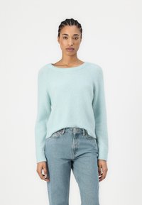 Lys blå strikkegenser med rund hals og ribbestrikkede mansjetter, båret med falmede blå denimjeans, som har en avslappet passform og lodden tekstur.