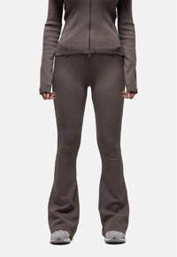 Ensemble en deux pièces marron à côtes comprenant une veste zippée et un legging évasé, avec une finition texturée. Porté avec des baskets grises.