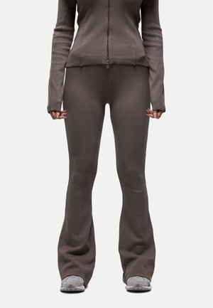 Completo a due pezzi marrone a coste con giacca con zip e leggings svasati, dal finish texture. Indossato con sneakers grigie.